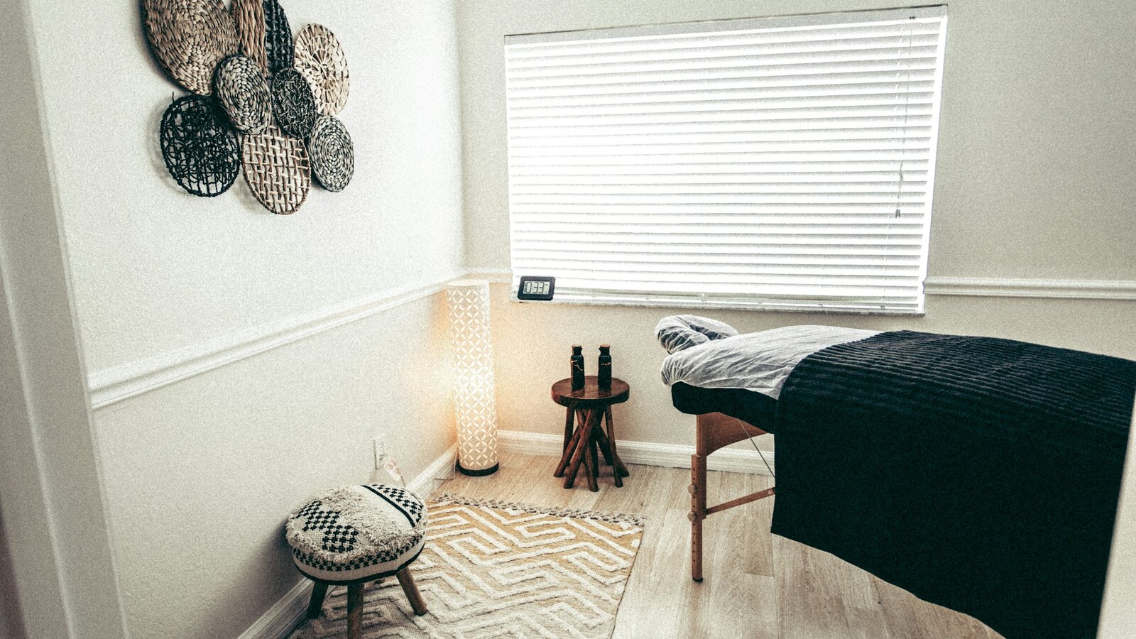 A calm treatment room with a massage table, wood floor and soft lamp